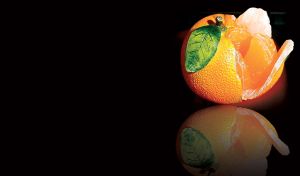 Half peeled fresh orange showing a slice of juicy fruit on black, reflected below
