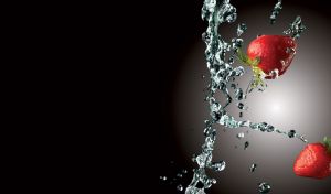 Two strawberries falling next to pouring water splash on black with white backlight
