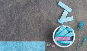 Sticks of blue bubble gum and dried blue flowers on a textured grey backdrop