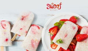 Ice pops and strawberries against a pastel white-blue wooden table