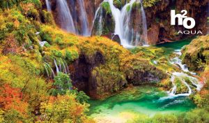 Emerald river flows by the green grassy rock surrounded by cliffs and waterfalls