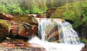 Waterfall drizzles onto the moss-covered red rocks in a green summer forest