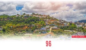 Summer village on a green hill beneath white clouds in the blue sky on white