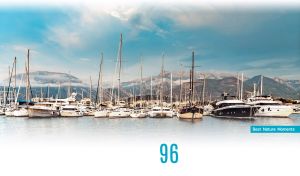 Marina with boats by the mountains under the light blue sky on white