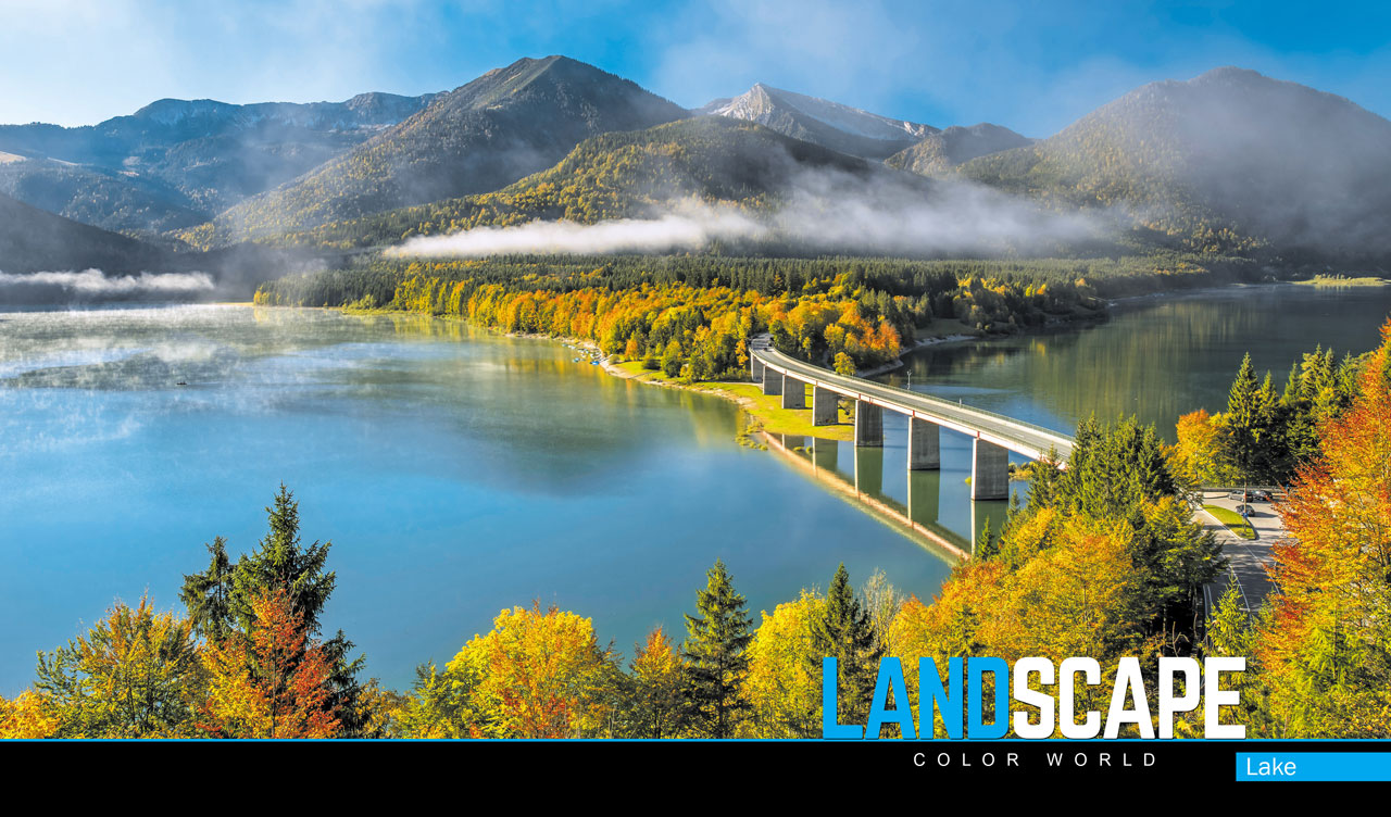 Panoramic view of a bridge over a mountain lake leading into a misty forest