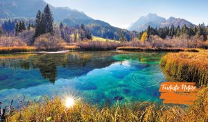 Tranquil lake set against a backdrop of hazy mountains and a dense fir forest