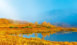 Golden autumn valley with clear blue lake against blue-white gradient sky
