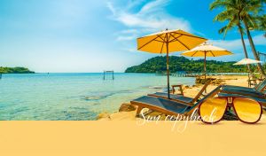 Tropical scene with beach loungers and palm trees by the blue ocean