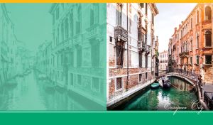 Gondolas pass under a bridge along a canal between the lined buildings in Venice
