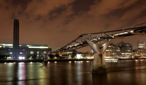 Steel bridge on a dark river in the city lights of modern buildings