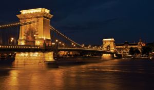Chain bridge on a dark river in the bright city lights of historical buildings