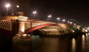 Metal bridge with street lights on a dark river in the city lights of buildings