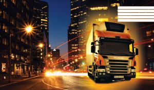 Orange yellow truck drives through the night city leaving high-speed lights on the road